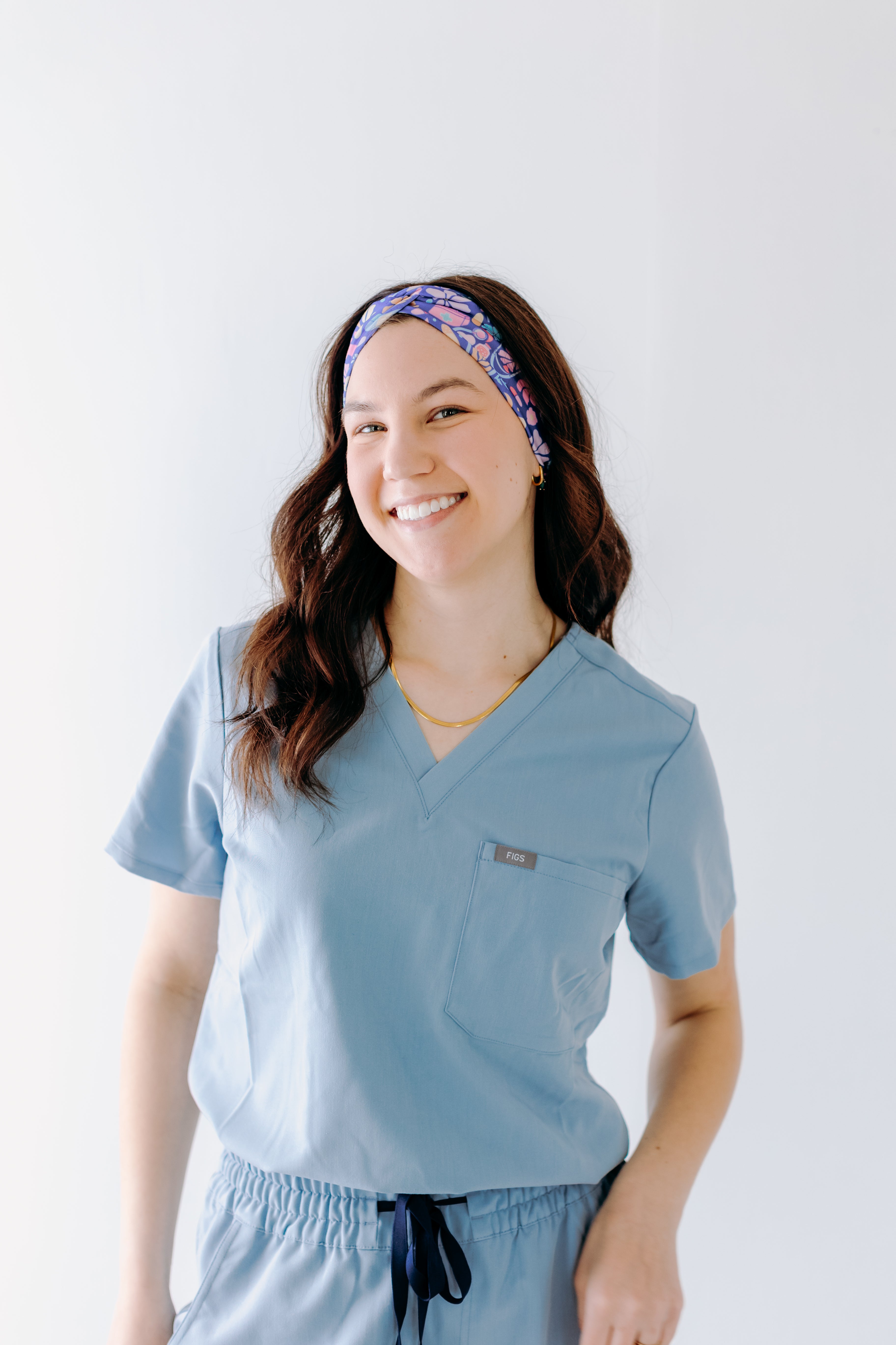 A nurse smiling with long hair while wearing the Ask Us About Our Warm Blankets headband for cute hairstyles and comfortable all-day wear.