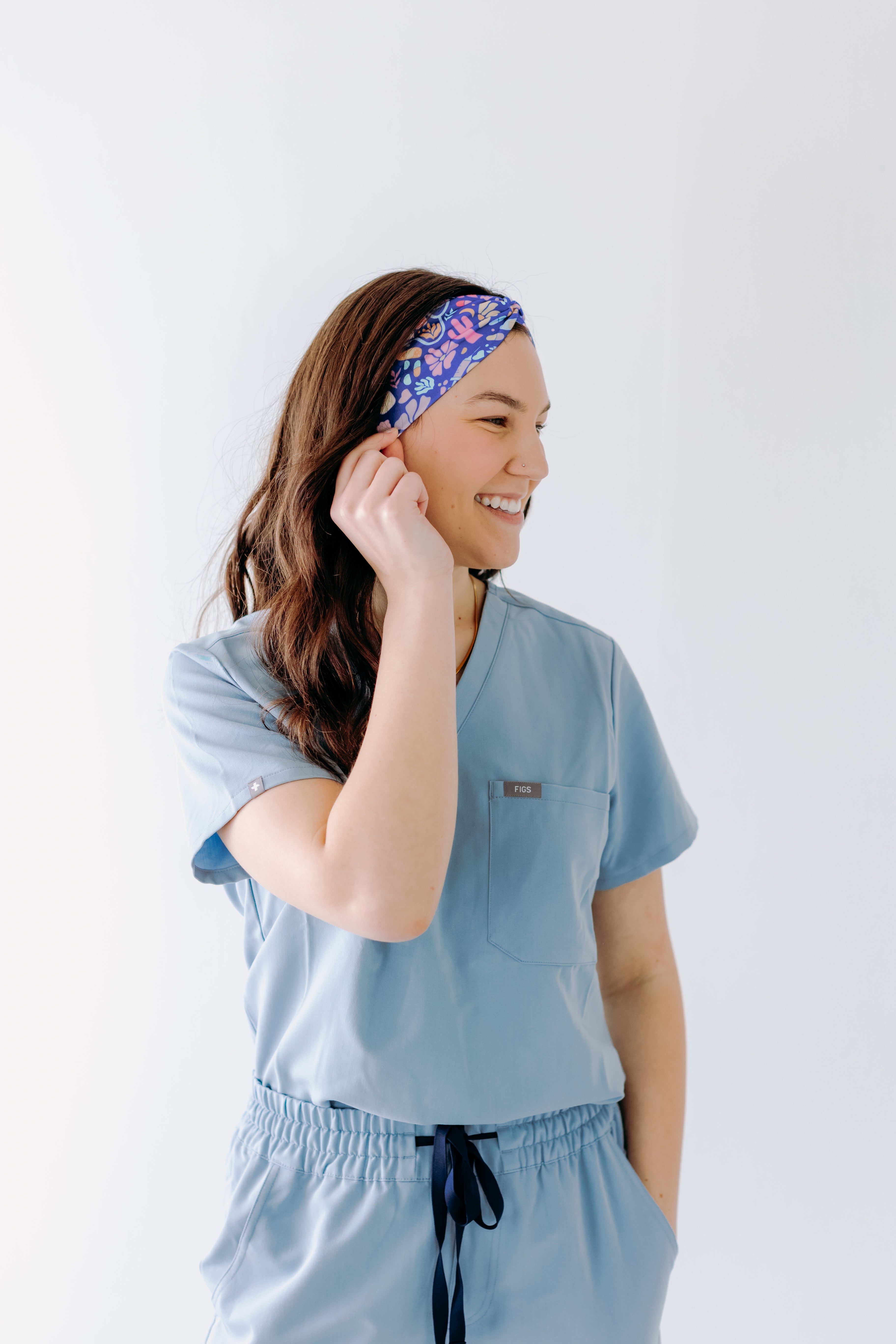 A nurse smiling with long hair while wearing the Ask Us About Our Warm Blankets headband for cute hairstyles and comfortable all-day wear.