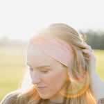 Woman smiling, wearing a Spiced Peach headband, showcasing its versatility and comfort, ideal for workouts or casual wear, made from soft, stretchy poly-knit blend.