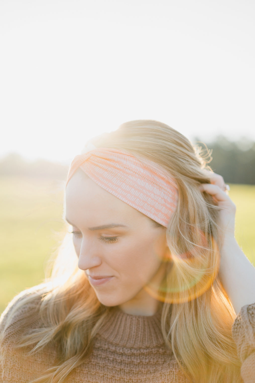 Woman smiling, wearing a Spiced Peach headband, showcasing its versatility and comfort, ideal for workouts or casual wear, made from soft, stretchy poly-knit blend.