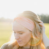 Woman smiling, wearing a Spiced Peach headband, showcasing its versatility and comfort, ideal for workouts or casual wear, made from soft, stretchy poly-knit blend.