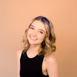 A woman wearing the Chloe Floral on Black headband, smiling with her hand on her head, showcasing its functional and versatile design.