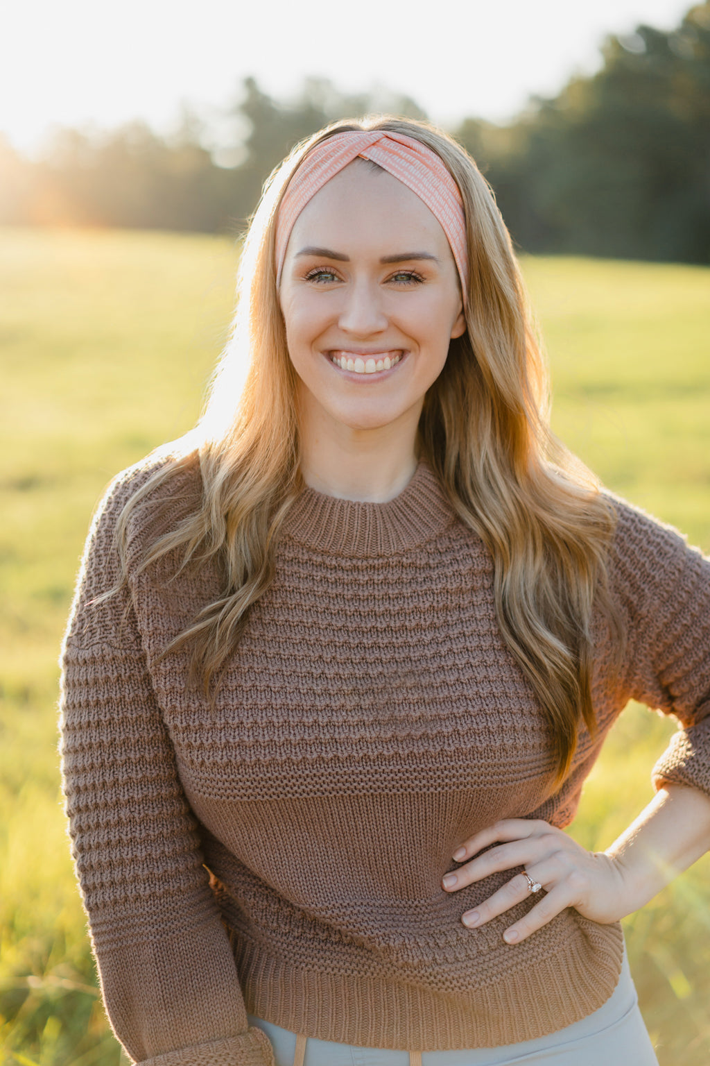 Woman smiling, wearing a Spiced Peach headband, showcasing its versatility and comfort, ideal for workouts or casual wear, made from soft, stretchy poly-knit blend.