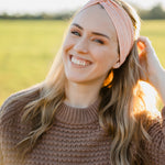 Woman smiling, wearing a Spiced Peach headband, showcasing its versatility and comfort, ideal for workouts or casual wear, made from soft, stretchy poly-knit blend.