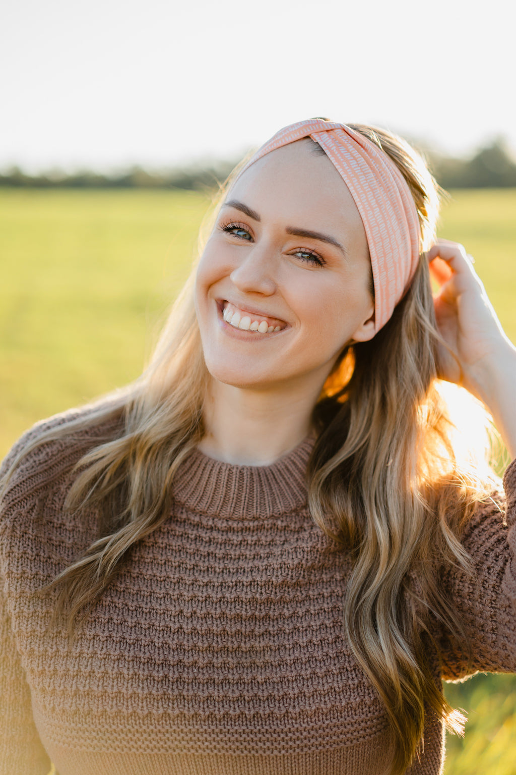 Woman smiling, wearing a Spiced Peach headband, showcasing its versatility and comfort, ideal for workouts or casual wear, made from soft, stretchy poly-knit blend.