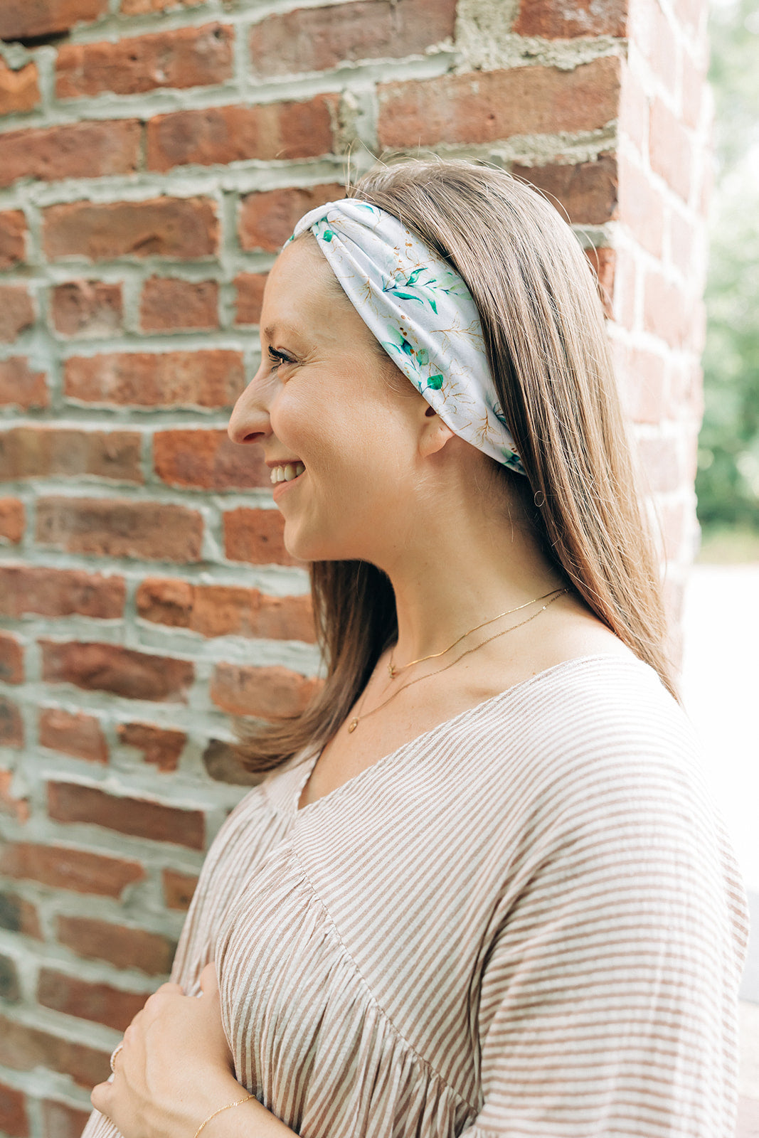 A woman smiling and confidently wearing the Springtime in Brooklyn headband from The Sarah Wallace Collection, showcasing its versatile twist style and non-slip design.