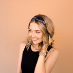 A woman wearing the Chloe Floral on Black headband, smiling with her hand on her head, showcasing its functional and versatile design.