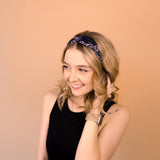 A woman wearing the Chloe Floral on Black headband, smiling with her hand on her head, showcasing its functional and versatile design.