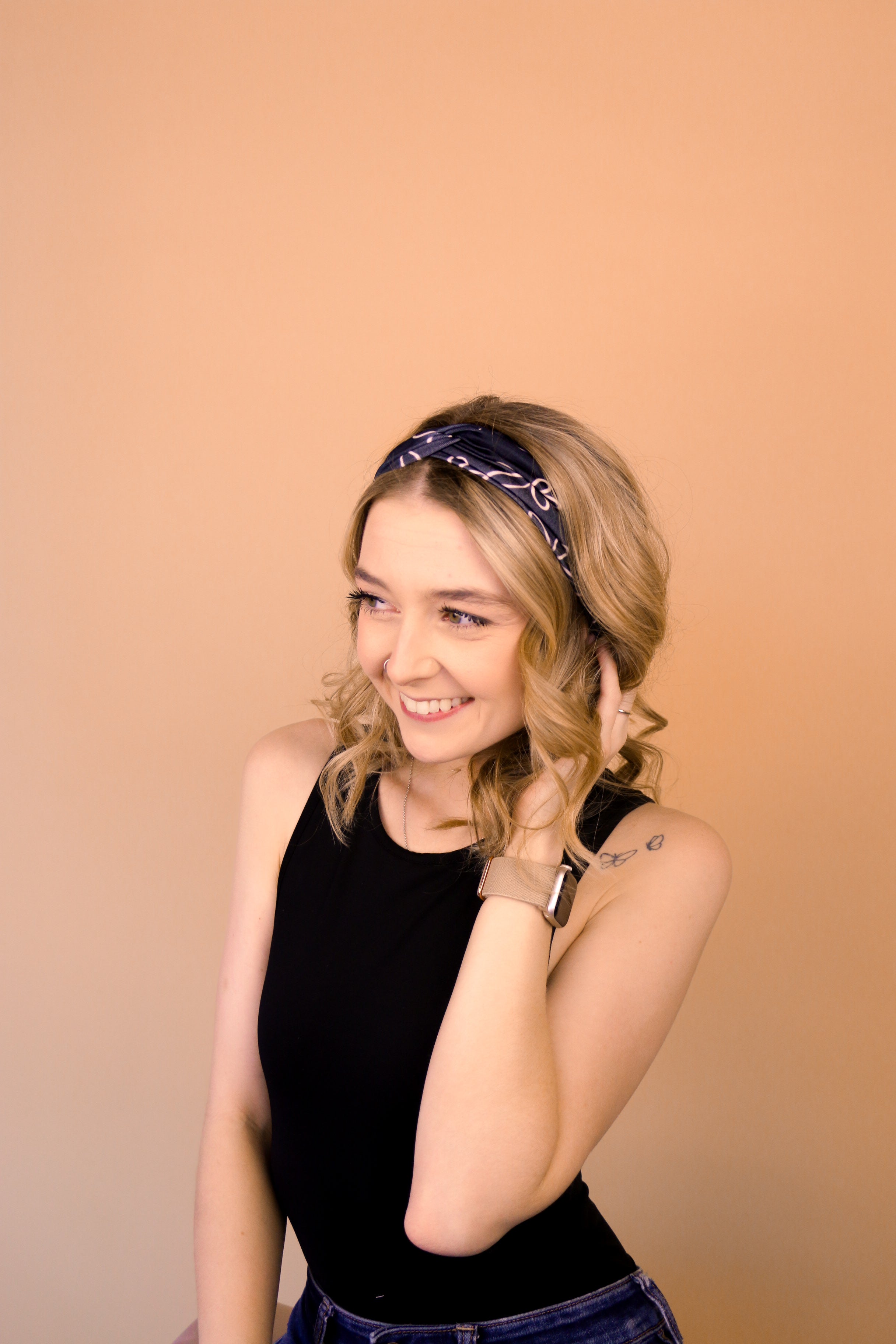 A woman wearing the Chloe Floral on Black headband, smiling with her hand on her head, showcasing its functional and versatile design.