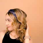 A woman wearing the Chloe Floral on Black headband, smiling with her hand on her head, showcasing its functional and versatile design.
