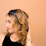 A woman wearing the Chloe Floral on Black headband, smiling with her hand on her head, showcasing its functional and versatile design.
