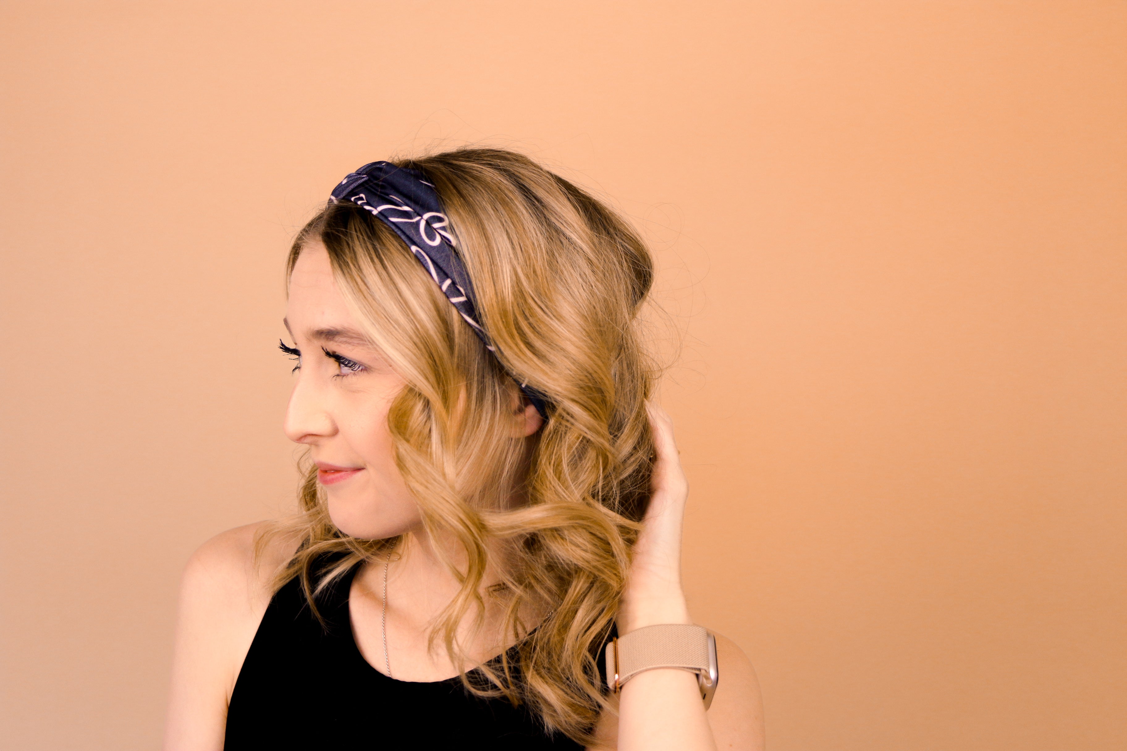 A woman wearing the Chloe Floral on Black headband, smiling with her hand on her head, showcasing its functional and versatile design.