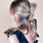 A woman wearing the Effortless Lilac Clip, a glossy hair accessory, in a dress with long hair.