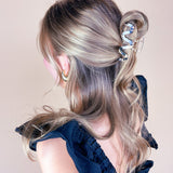 A woman wearing the Effortless Lilac Clip, a glossy hair accessory, in a dress with long hair.