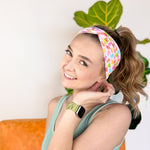 A woman wearing the hair accessory Don't Be Jelly headband with colorful jelly bean pattern, perfect for workouts, long shifts, and play days.