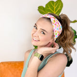 A woman wearing the hair accessory Don't Be Jelly headband with colorful jelly bean pattern, perfect for workouts, long shifts, and play days.