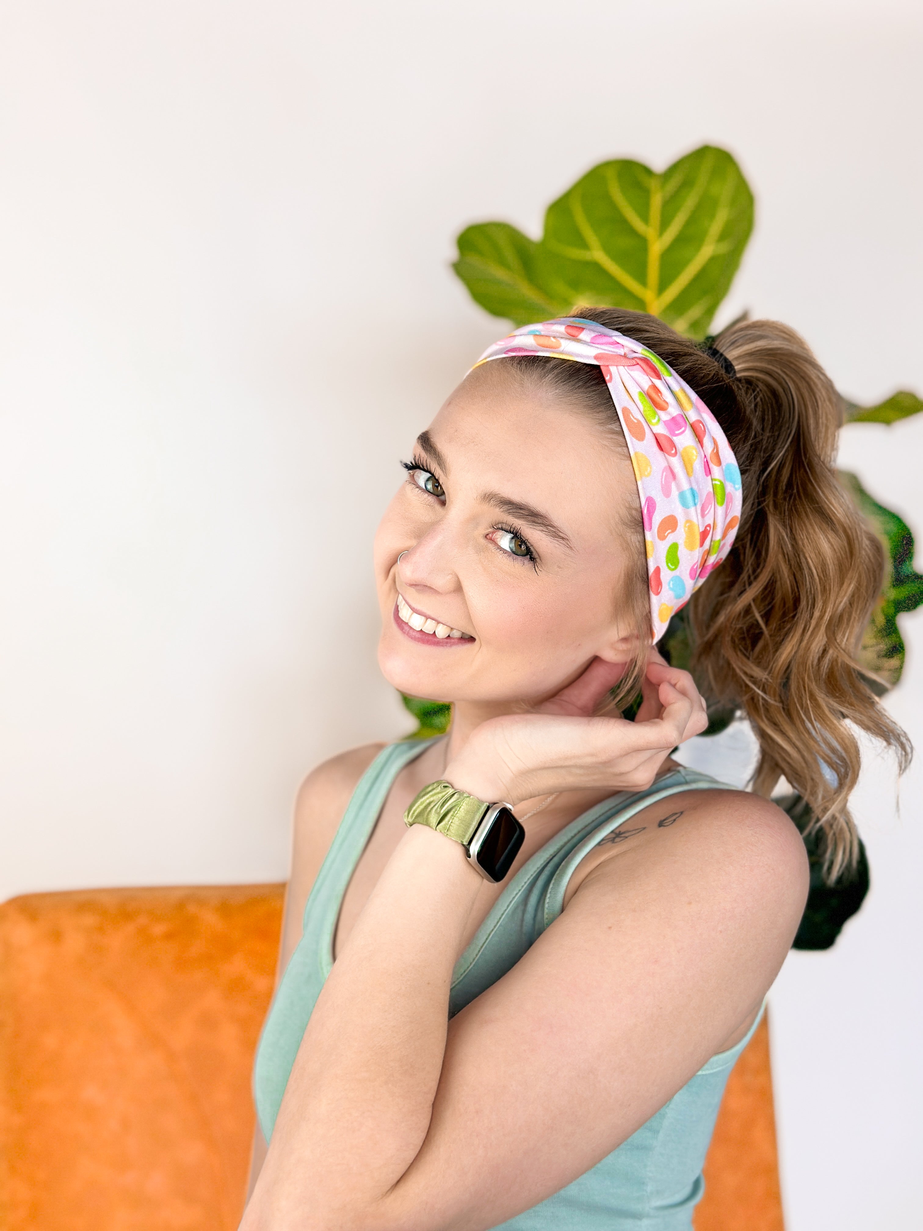 A woman wearing the hair accessory Don't Be Jelly headband with colorful jelly bean pattern, perfect for workouts, long shifts, and play days.