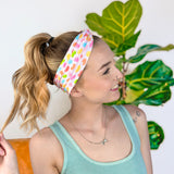 A woman wearing the hair accessory Don't Be Jelly headband with colorful jelly bean pattern, perfect for workouts, long shifts, and play days.