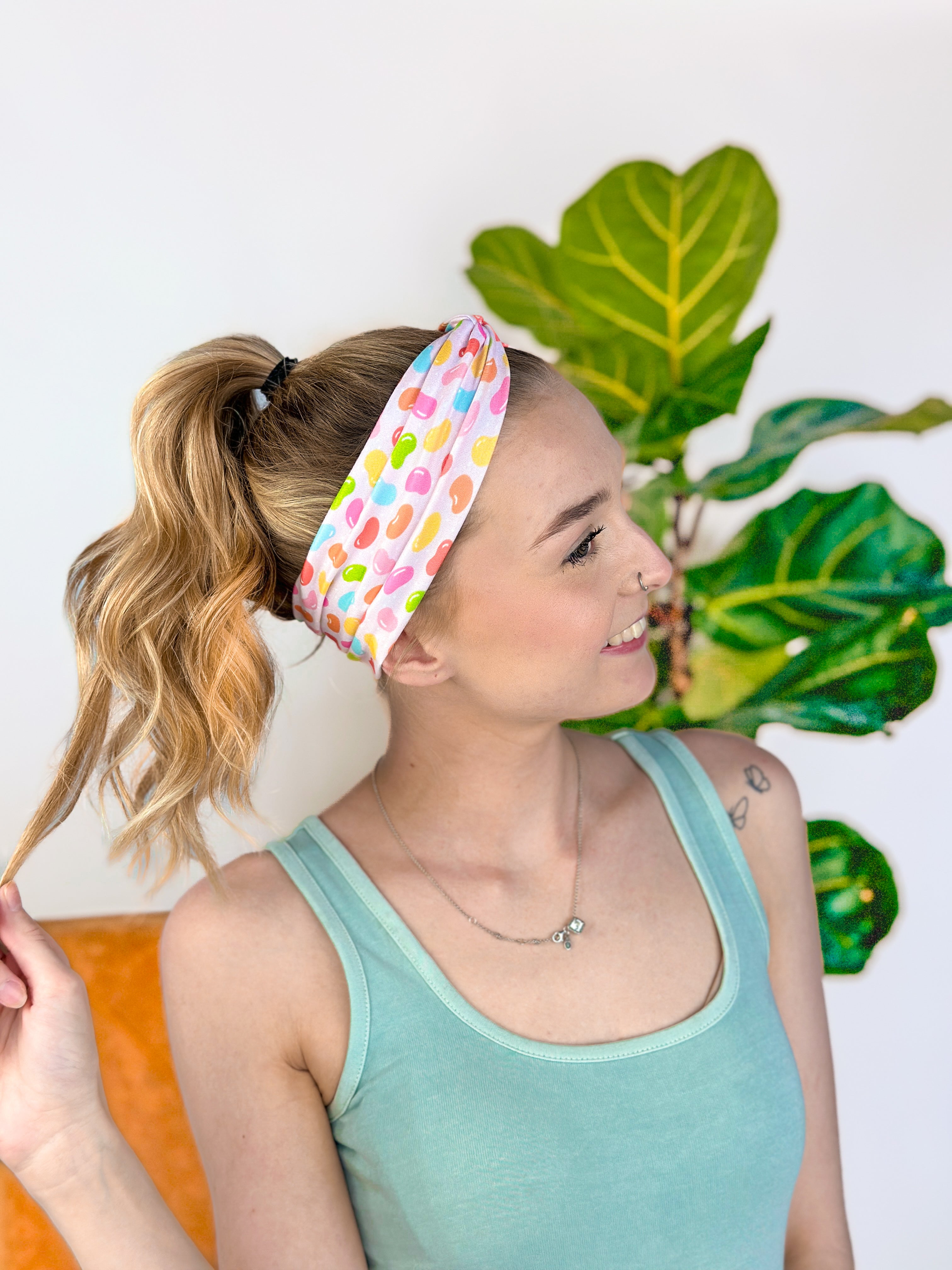 A woman wearing the hair accessory Don't Be Jelly headband with colorful jelly bean pattern, perfect for workouts, long shifts, and play days.