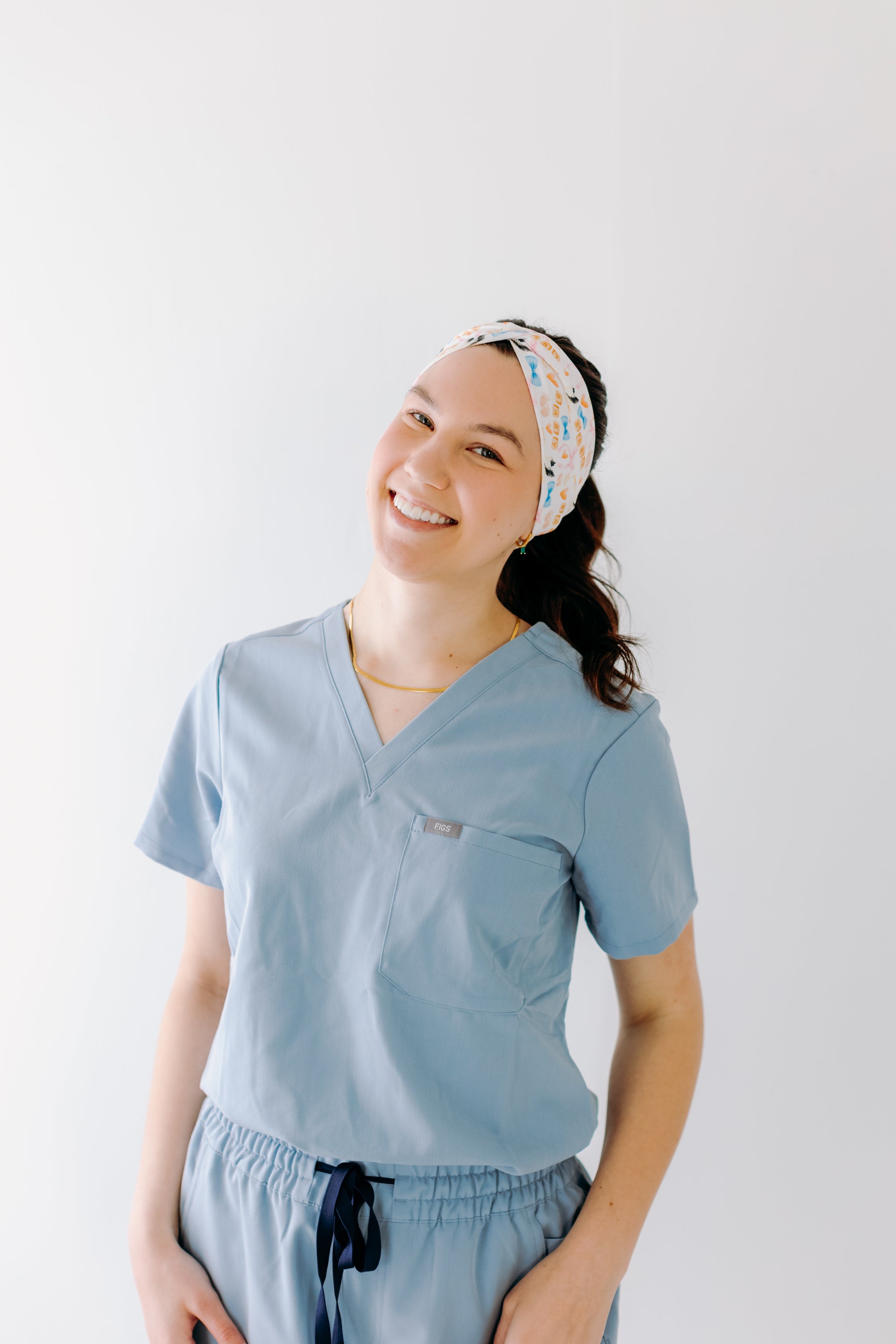 A nurse smiling with a long ponytail while wearing the It's A Great Day in the Laborhood headband for cute hairstyles and comfortable all-day wear.