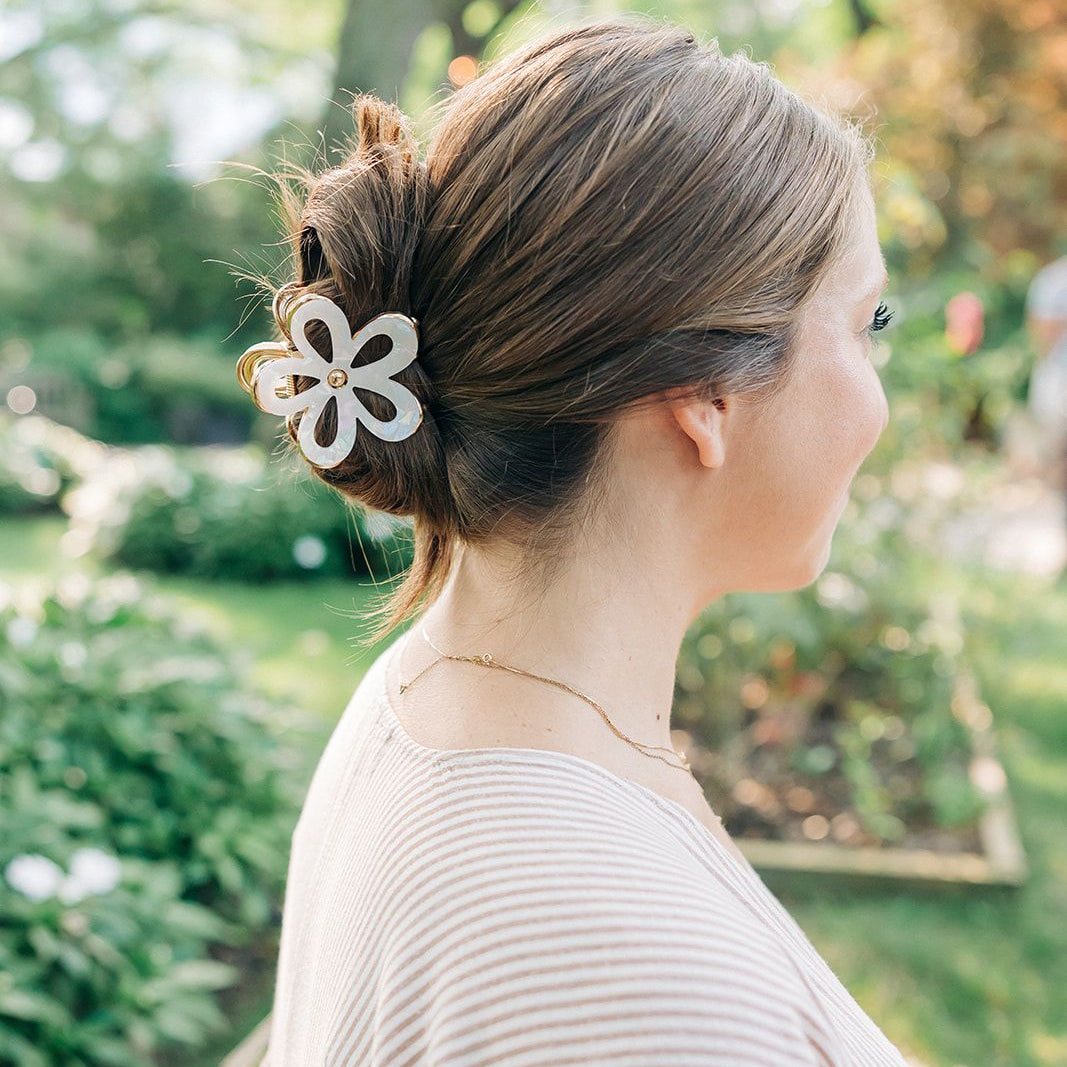 Woman outdoors with a white flower Central Park Stroll Clip. Holding her bun securely, her style highlights the clip's marble and metal design.