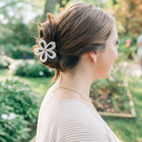 Woman outdoors with a white flower Central Park Stroll Clip. Holding her bun securely, her style highlights the clip's marble and metal design.