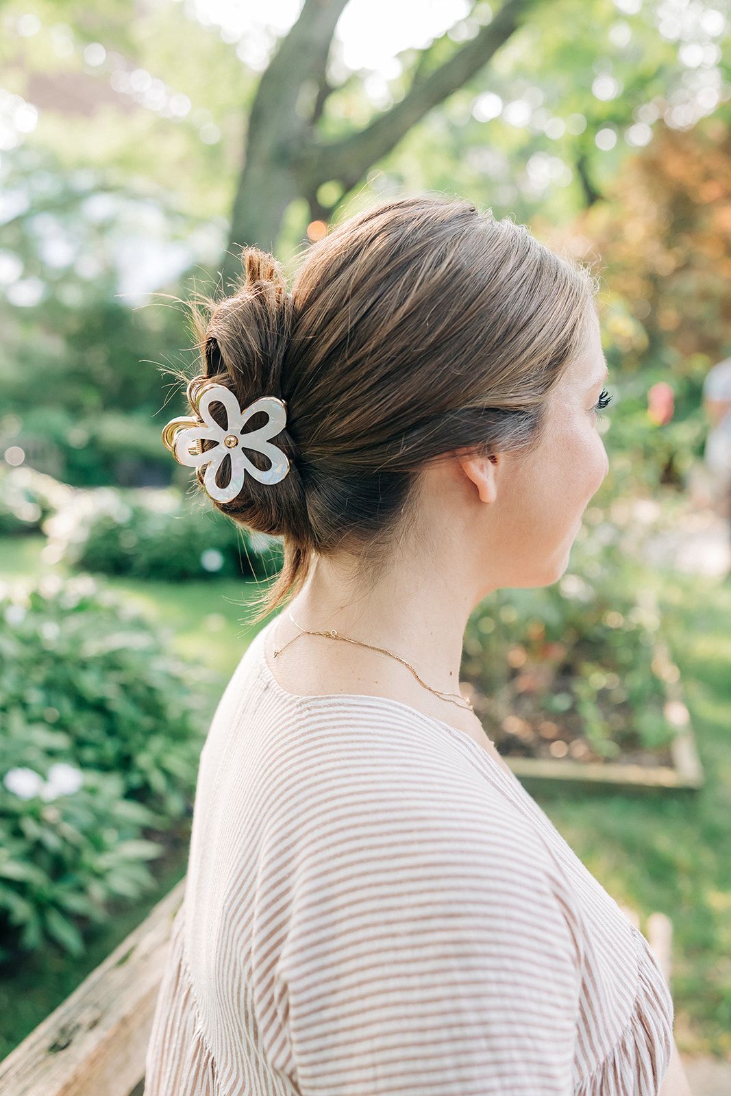 Woman outdoors with a white flower Central Park Stroll Clip. Holding her bun securely, her style highlights the clip's marble and metal design.