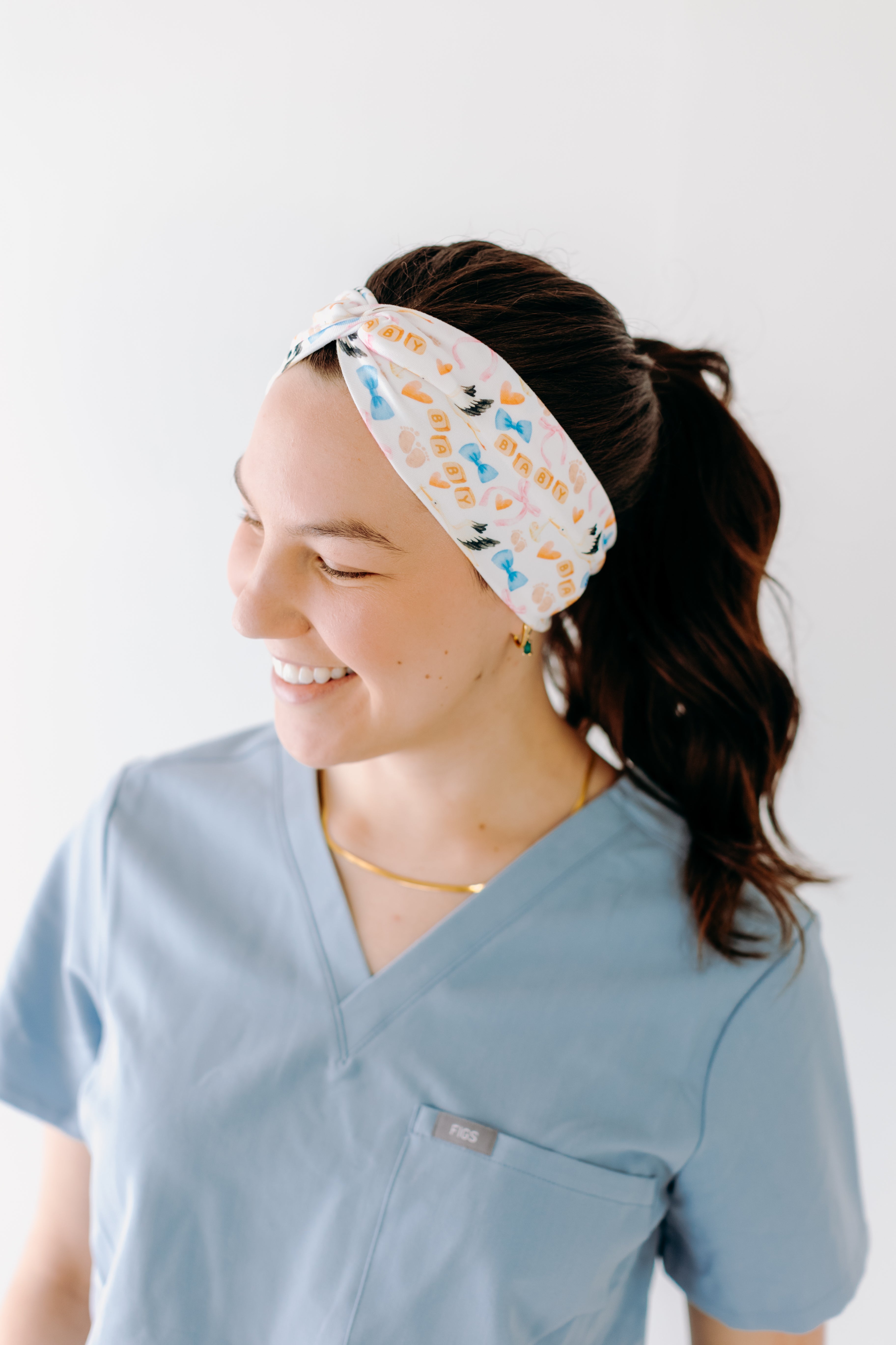 A nurse smiling with a long ponytail while wearing the It's A Great Day in the Laborhood headband for cute hairstyles and comfortable all-day wear.