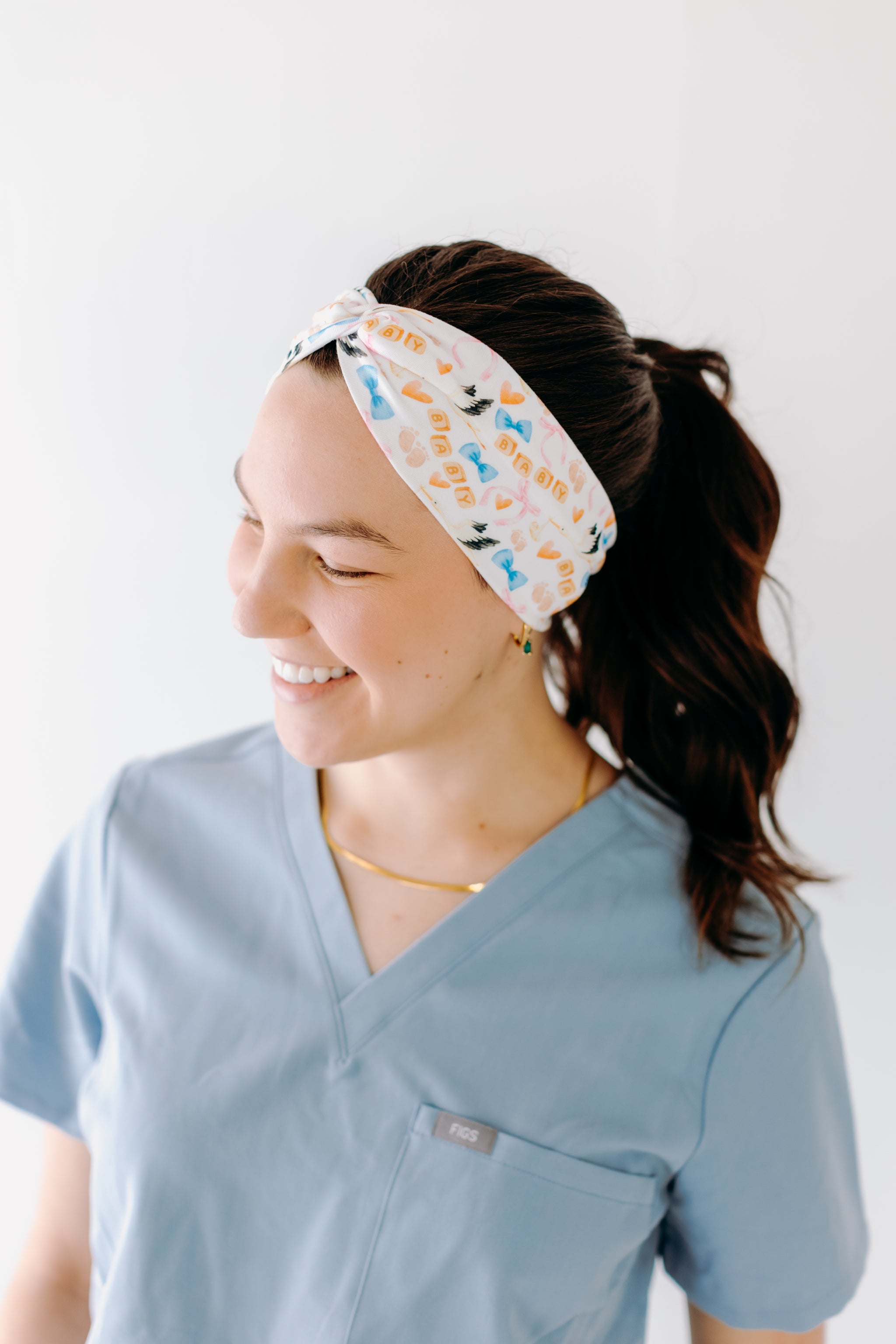 A nurse smiling with a long ponytail while wearing the It's A Great Day in the Laborhood headband for cute hairstyles and comfortable all-day wear.