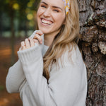 Autumn Daisy headband with purple and white flowers, worn by smiling woman, showcasing its versatile 3-in-1 twist style and cozy, stretchy poly-knit fabric.