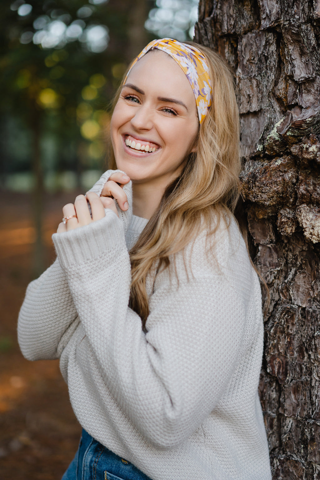 Autumn Daisy headband with purple and white flowers, worn by smiling woman, showcasing its versatile 3-in-1 twist style and cozy, stretchy poly-knit fabric.