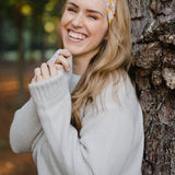 Autumn Daisy headband with purple and white flowers, worn by smiling woman, showcasing its versatile 3-in-1 twist style and cozy, stretchy poly-knit fabric.