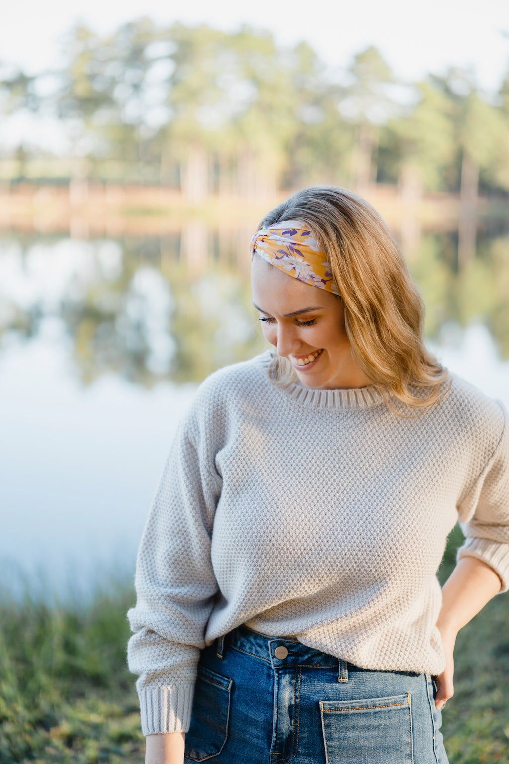 Autumn Daisy headband with purple and white flowers, worn by smiling woman, showcasing its versatile 3-in-1 twist style and cozy, stretchy poly-knit fabric.