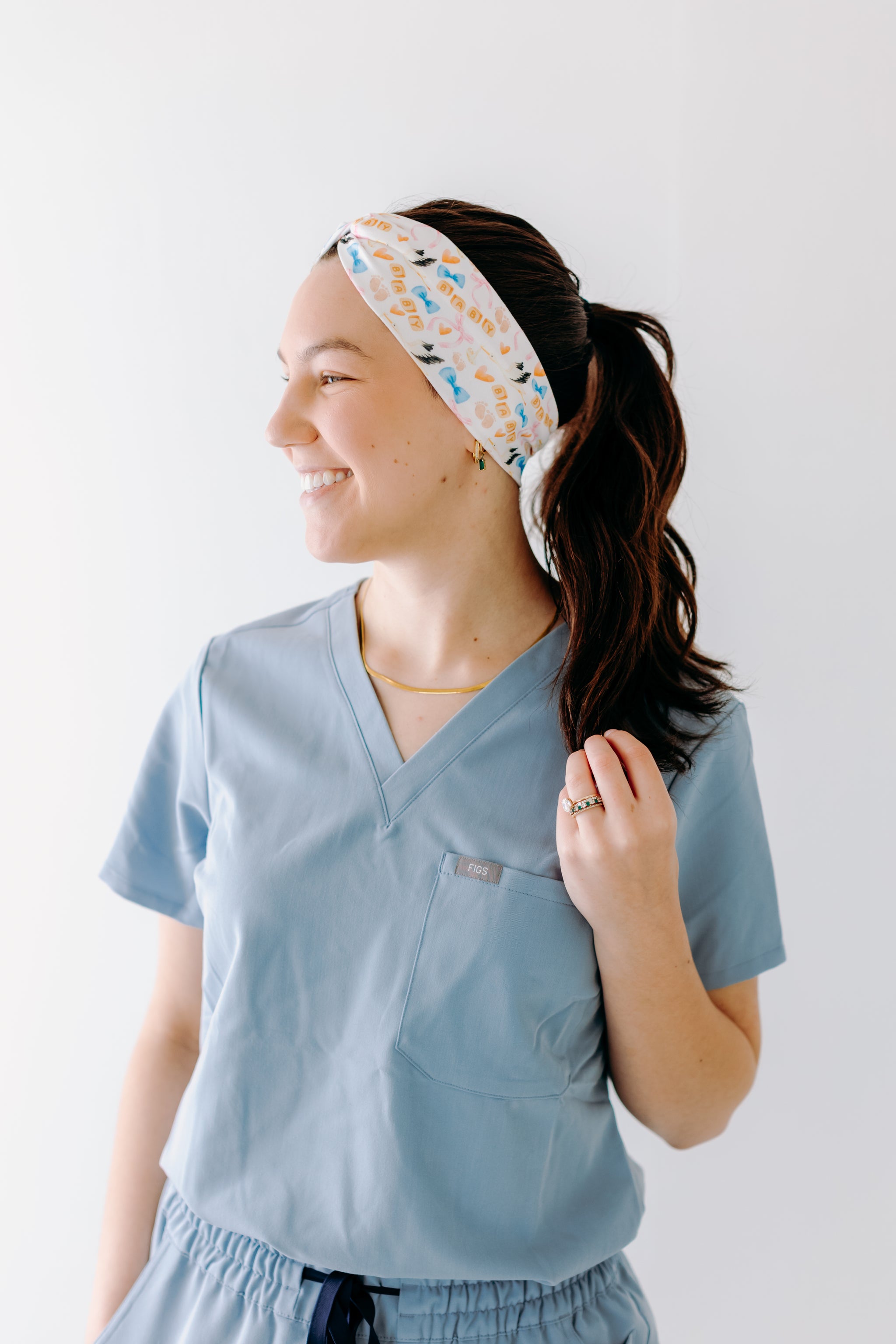 A nurse smiling with a long ponytail while wearing the It's A Great Day in the Laborhood headband for cute hairstyles and comfortable all-day wear.