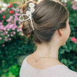 Woman wearing the Grow With Grace Clip from The Sarah Wallace collection, a 4.4-inch metal hair accessory with a flower design, securing her hair in a bun.