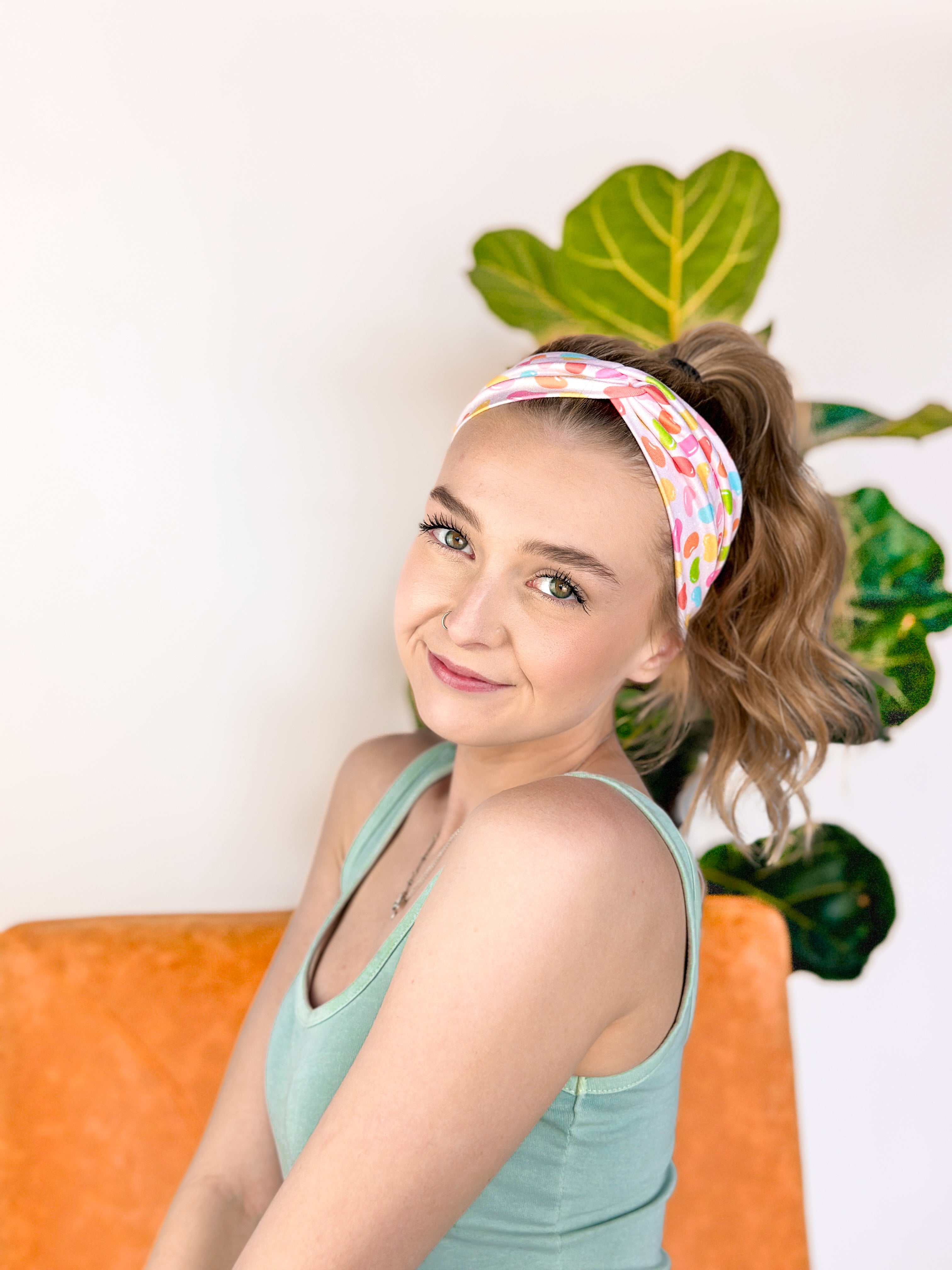 A woman wearing the hair accessory Don't Be Jelly headband with colorful jelly bean pattern, perfect for workouts, long shifts, and play days.
