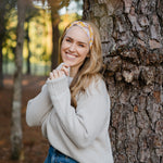 Autumn Daisy headband with purple and white flowers, worn by smiling woman, showcasing its versatile 3-in-1 twist style and cozy, stretchy poly-knit fabric.