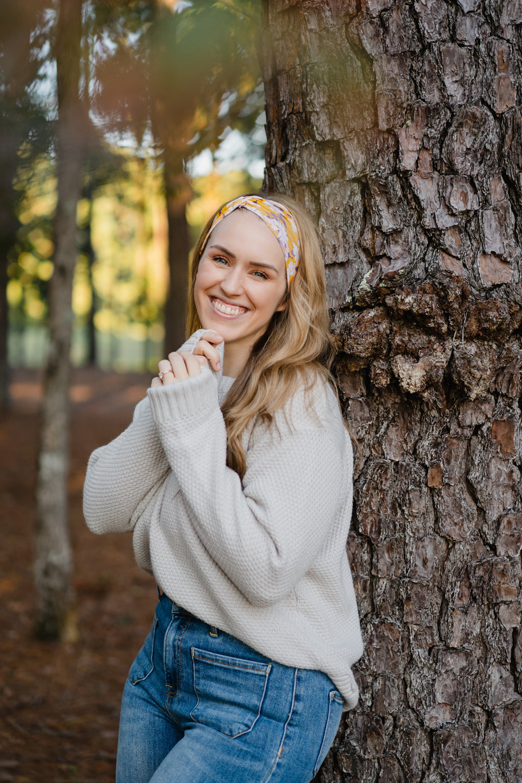 Autumn Daisy headband with purple and white flowers, worn by smiling woman, showcasing its versatile 3-in-1 twist style and cozy, stretchy poly-knit fabric.