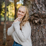 Autumn Daisy headband with purple and white flowers, worn by smiling woman, showcasing its versatile 3-in-1 twist style and cozy, stretchy poly-knit fabric.