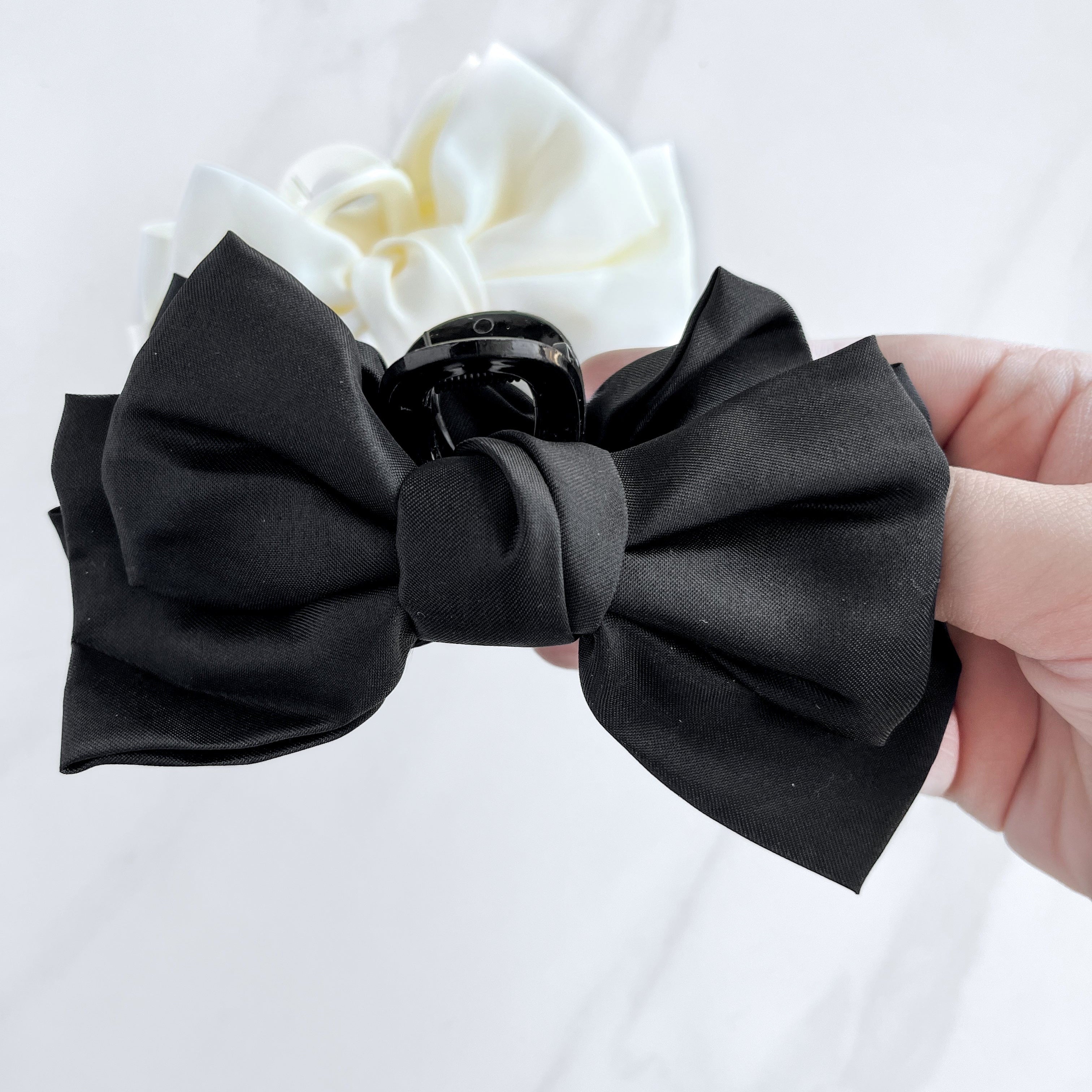 A hand holding a Classy Chic Lilac Clip, a perfect claw clip for all hair types and textures, made of silky black satin material with a hinge closure.