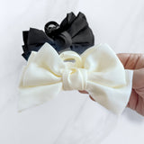 A hand holding a Classy Chic Lilac Clip, a perfect claw clip for all hair types and textures, made of silky white satin material with a hinge closure.