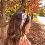 Woman smiling outdoors wearing It's Giving Thanks headband, showcasing its versatile 3-in-1 twist style and non-slip design against a tree backdrop.