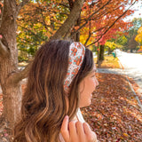 Woman smiling outdoors wearing It's Giving Thanks headband, showcasing its versatile 3-in-1 twist style and non-slip design against a tree backdrop.