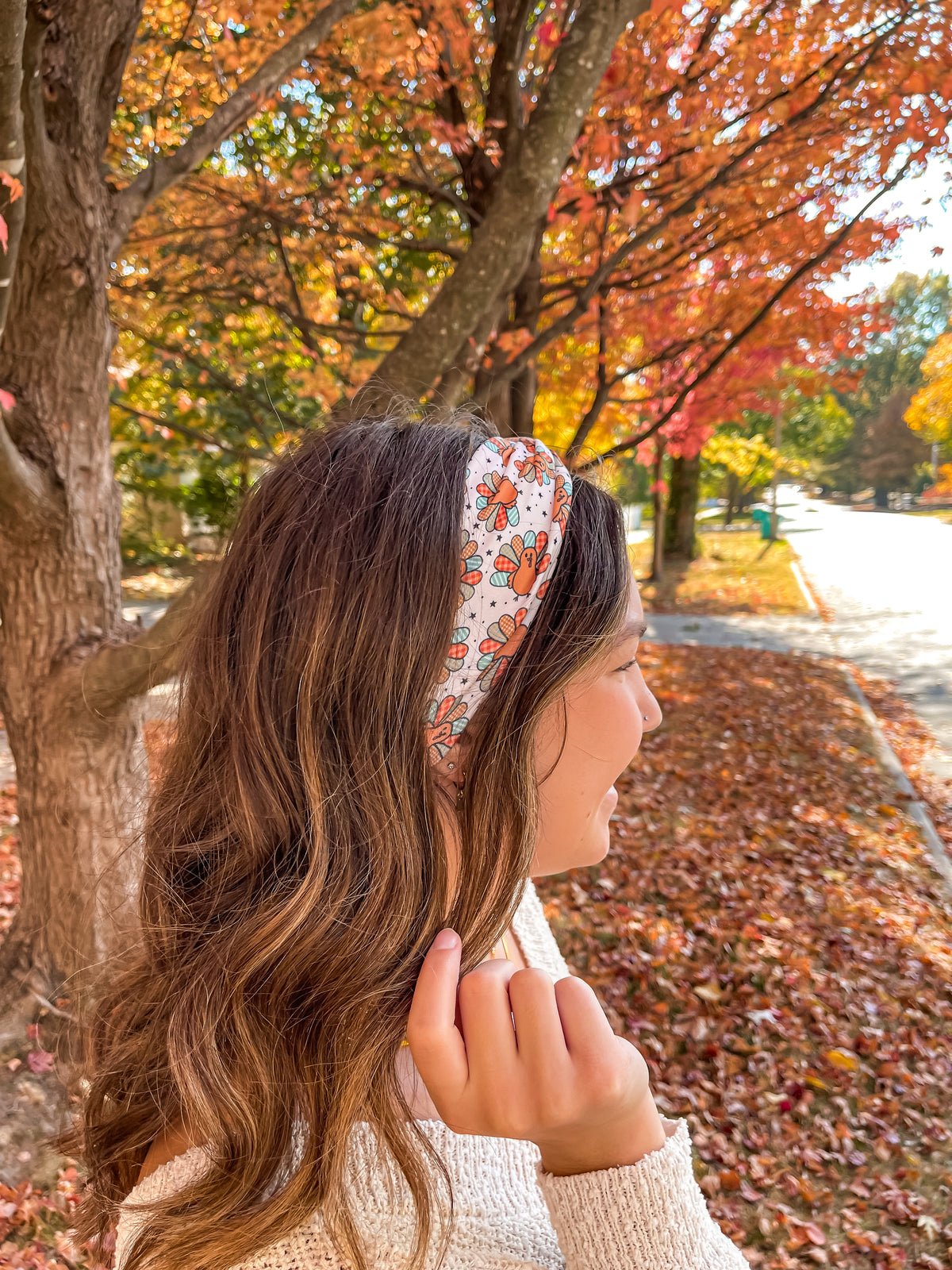 Woman smiling outdoors wearing It's Giving Thanks headband, showcasing its versatile 3-in-1 twist style and non-slip design against a tree backdrop.