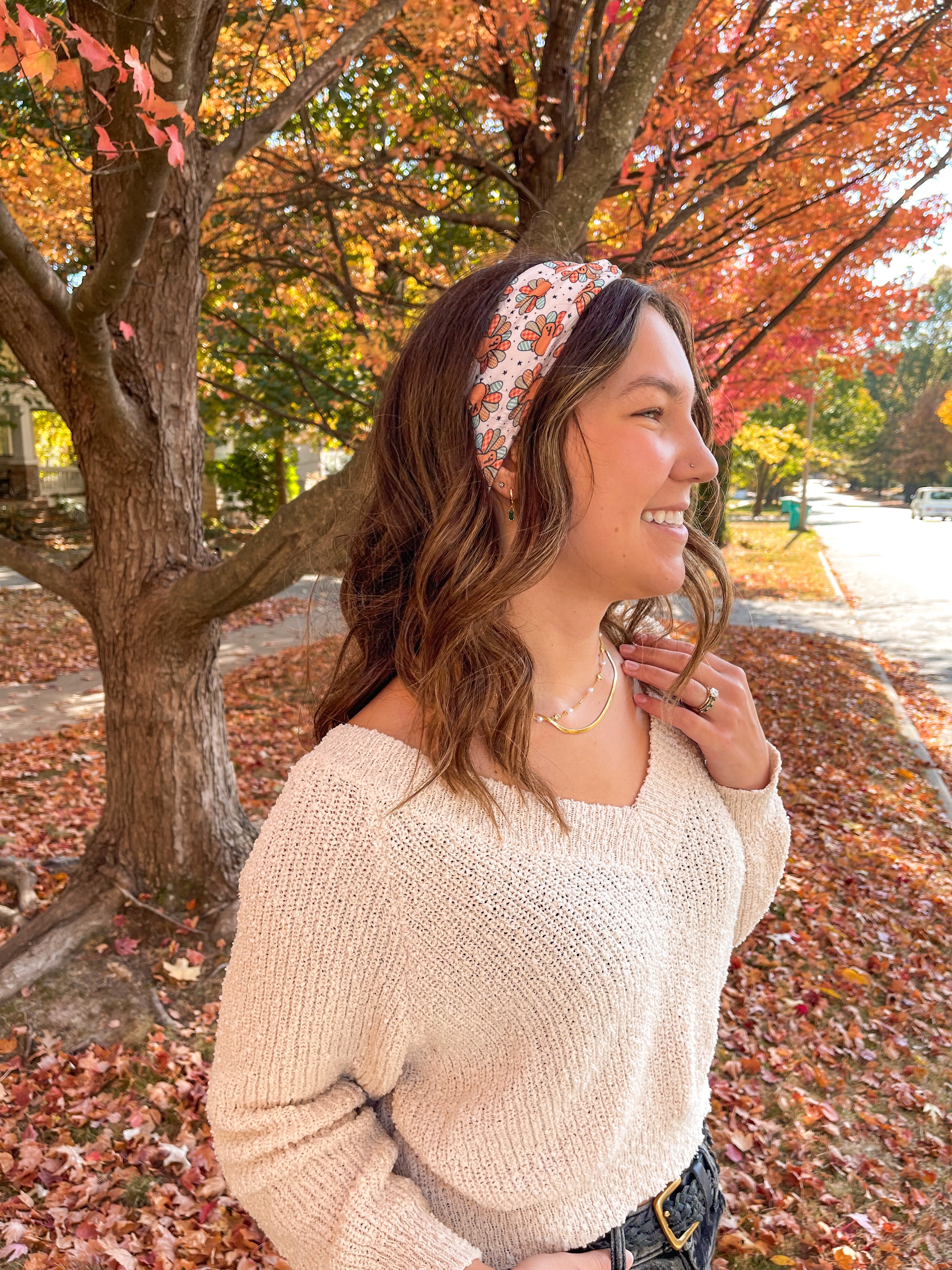 Woman smiling outdoors wearing It's Giving Thanks headband, showcasing its versatile 3-in-1 twist style and non-slip design against a tree backdrop.