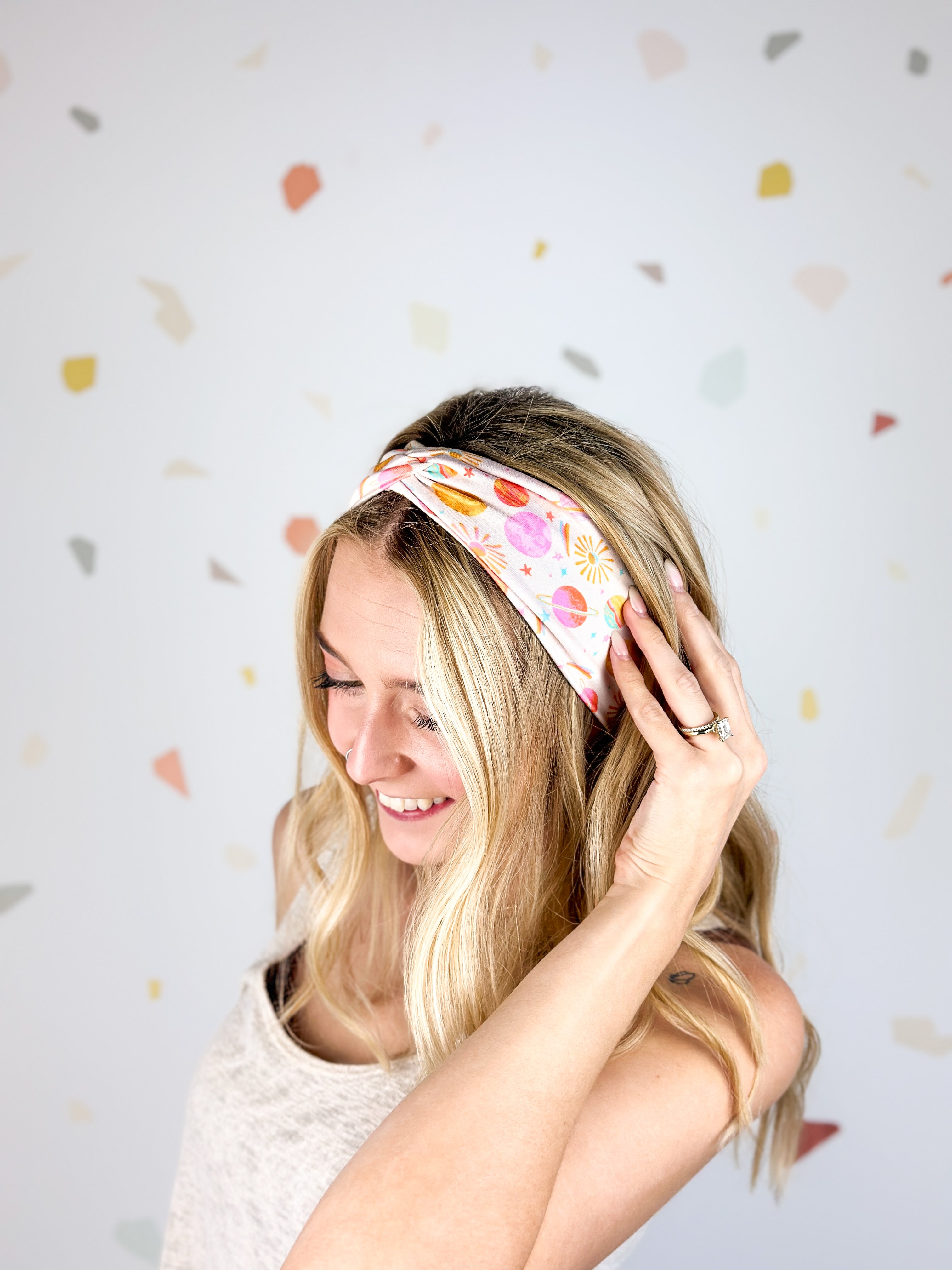 Woman smiling, wearing Field Trip to the Stars headband; ultra-stretchy, versatile, double-layered, non-slip, and sweat-absorbent. Ideal for workouts, long shifts, or playdays.