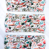 An Enchanted Garden headband with a mushroom and plant pattern, featuring a knot design. Versatile 3-in-1 twist style, sweat-absorbent, non-slip, and machine washable. Functional and stylish for any activity.