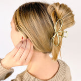 A woman wearing an Invisible String Lilac Clip in her hair, showcasing the shiny gold metal material and hinge closure. Perfect for all hair types, adding style effortlessly.