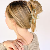 A woman wearing an Invisible String Lilac Clip in her hair, showcasing the shiny gold metal material and hinge closure. Perfect for all hair types, adding style effortlessly.