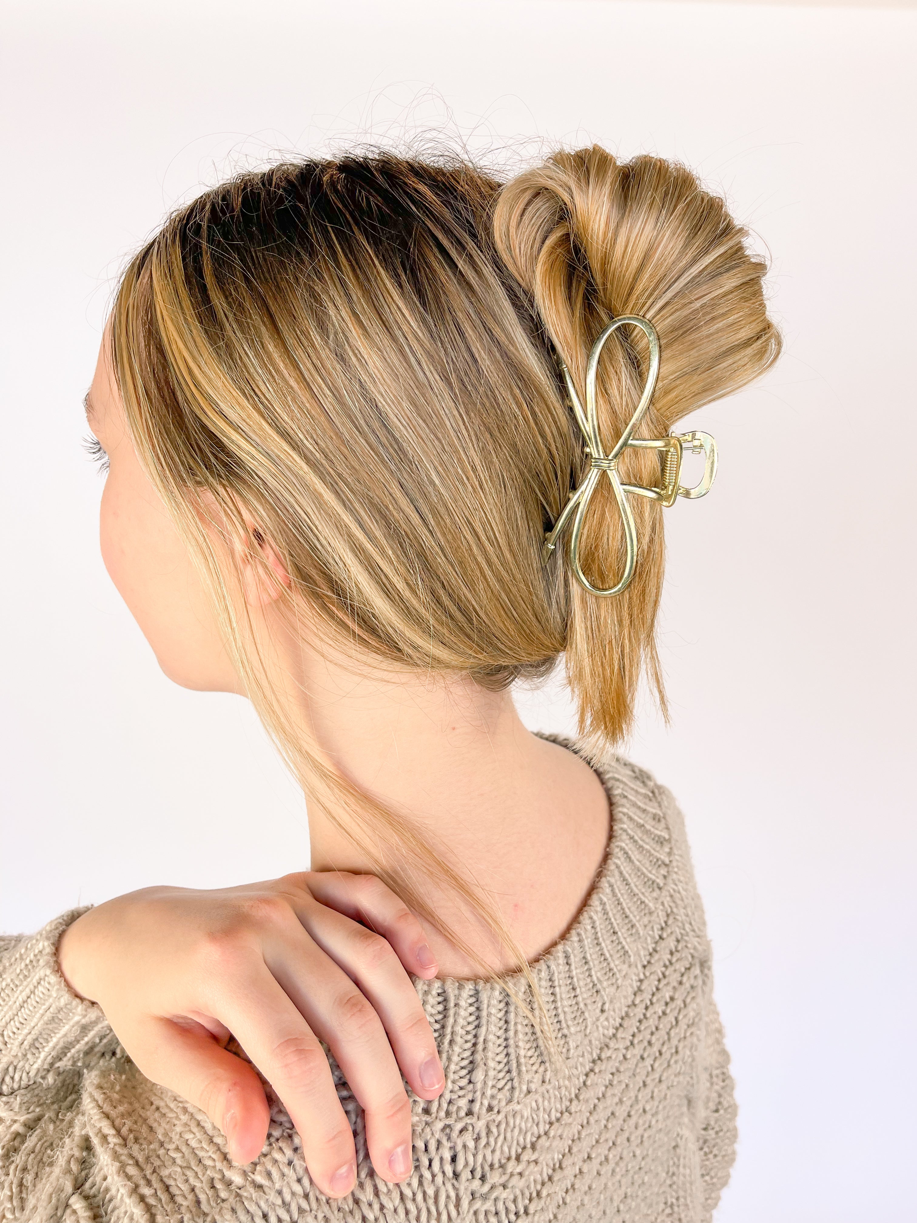 A woman wearing an Invisible String Lilac Clip in her hair, showcasing the shiny gold metal material and hinge closure. Perfect for all hair types, adding style effortlessly.